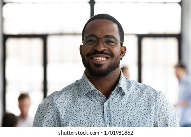Headshot portrait of smiling African American male employee in glasses look at camera posing at workplace, happy motivated biracial man worker show confidence and leadership, employment concept