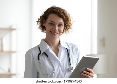 Headshot Portrait Of Smiling Caucasian Female Nurse In White Uniform Use Modern Tablet Gadget. Happy Woman Doctor Or GP Consult Patient Online On Pad Device. Medicine And Technology Concept.