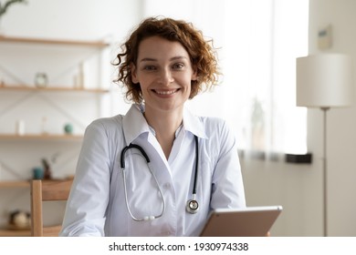 Headshot Portrait Of Smiling Caucasian Female Doctor Or GP Look At Camera Consult Patient On Tablet Online. Happy Young Woman Nurse Use Pad For Webcam Consultation. Virtual Event, Medicine Concept.