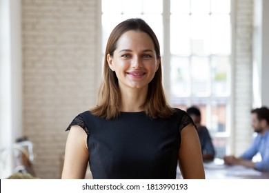 Headshot Portrait Of Smiling Millennial Businesswoman Stand Forefront In Office Look At Camera Posing, Happy Confident Young Caucasian Female Employee Or Company Boss CEO Show Confidence In Boardroom