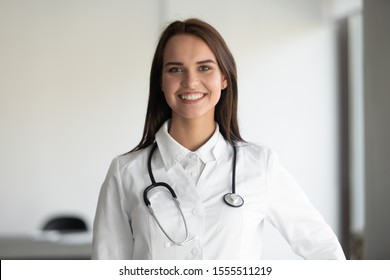 Headshot Portrait Of Smiling Millennial Female Doctor Wearing Medical Uniform And Stethoscope Looking At Camera, Happy Young Woman General Practitioner Or Nurse Posing In White, Healthcare Concept