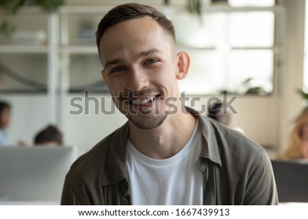 Headshot portrait of smiling millennial male employee talk on video call or web conference in coworking office, profile picture of happy Caucasian young man worker posing in shared workplace