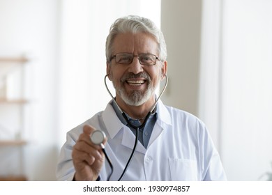 Headshot Portrait Of Smiling Senior Caucasian Male Doctor In White Medical Uniform Use Stethoscope. Profile Picture Of Happy Mature Man GP Or Therapist Examine Patient In Hospital. Healthcare Concept.