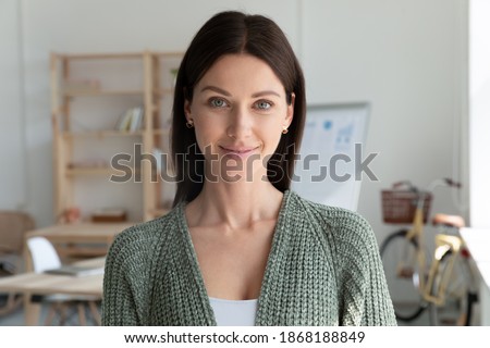 Headshot portrait of smiling young 20s businesswoman stand posing in modern office. Profile picture of happy female employee or worker show leadership and success at workplace. Employment concept.