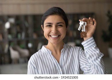 Headshot portrait of smiling young Indian woman hold show keys to new home or apartment. Profile picture of happy ethnic female renter or tenant celebrate moving relocation to own house. Rent concept.