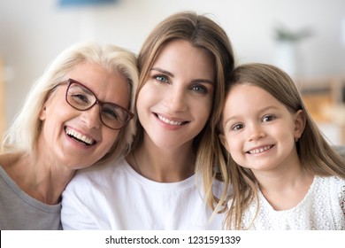 Headshot portrait of three 3 generations family, smiling grandmother, grown young daughter and child girl looking at camera, happy kid granddaughter, mother and old aged grandma posing together