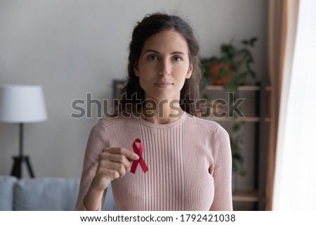 Headshot portrait of young Caucasian woman hold red ribbon breast cancer symbol support sick people patients, profile picture of millennial female raise HIV AIDS disease awareness, healthcare concept