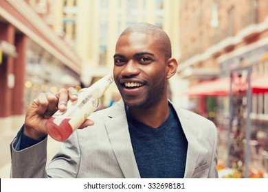 Headshot Portrait Of Young Smiling Man Drinking Soda From Glass Bottle Isolated On Outside Outdoors Urban Street Background.