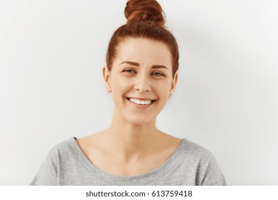 Headshot Of Relaxed Young Ginger Female Hipster With Perfect Beautiful Smile Looking With Happy Expression At Camera, Rejoicing At Her Carefree Lifestyle, Posing Indoors Against White Wall Background