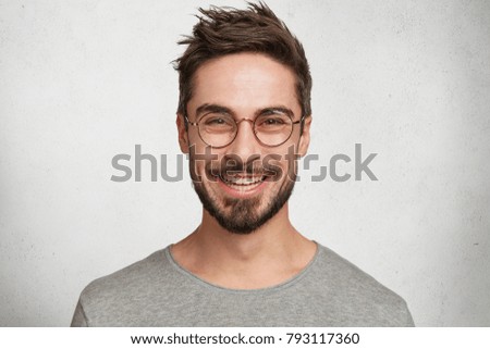 Headshot of satisfied cheerful handsome man grins at camera, glad to find suitable well paid job, isolated over white concrete background. People, positive emotions and facial expressions concept