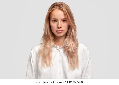 Headshot Of Self Assured Caucasian Female With Healthy Pure Skin, Wears Loose White Shirt, Looks Directly Into Camera, Has Serious Expression, Contemplates About Future Plans. Beauty And Lifestyle