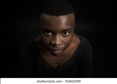 Headshot of serious confident young dark-skinned male standing isolated against black studiobackground.