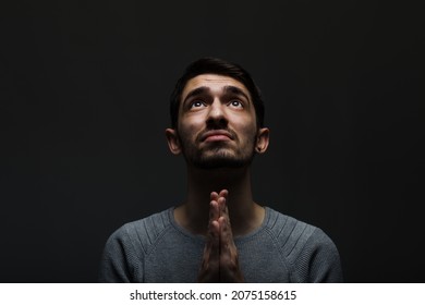 Headshot Of Serious Confident Young Man Praying In Dark Room. Lit From Above And Looking Up.