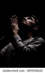 Headshot Of Serious Confident Young Man Praying In Dark Room. Lit From Above And Looking Up.