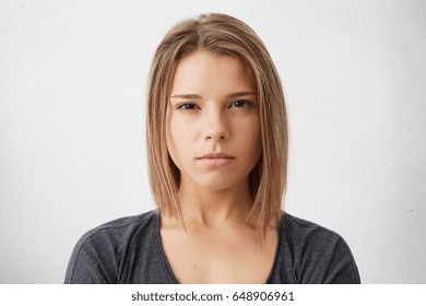 Headshot Of Serious Young Mixed Race Female Wearing Dark T-shirt Looking At Camera, Her Eyes Full Of Distrust And Disappoinment As She Has Quarrel With Boyfriend, Standing Isolated At Studio Wall