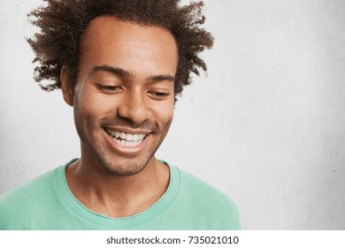 Headshot Of Shy Dark Skinned Male With Crisp Hair, Smiles Broadly, Shows White Even Teeth, Looks Down, Feels Embarassed As Sees Very Beautiful Woman, Wants To Make Compliment Or Get Acquainted