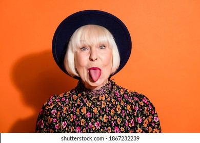 Headshot of sly funny crazy granny showing tongue careless childish playful isolated vibrant orange color background