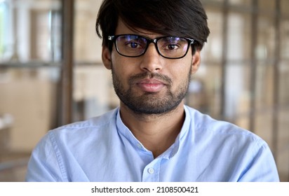 Headshot Of Young Adult Indian Arab Business Man Wearing Glasses Looking At Camera Posing In Office. Sales Manager, Professional Leader, Company Employee Or Entrepreneur Close Up Portrait.