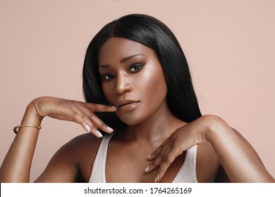 Headshot of young black afro female model, having nude make-up, with dark long hair over beige background.