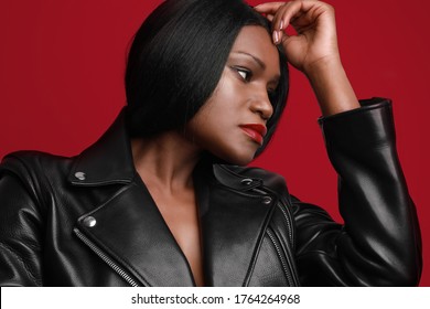 Headshot Of Young Black Female Model Looking Aside, Wearing Biker Jacket Posing Over Red Wall. Studio Shot.