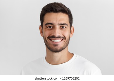 Headshot of young handsome european caucasian man isolated on gray background, smiling happily and friendly at camera, wearing casual white t-shirt, looking confident and relaxed