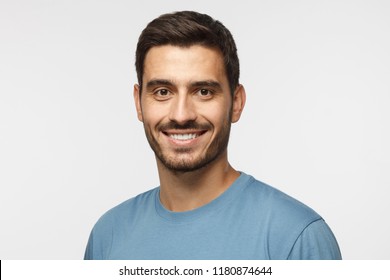 Headshot of young handsome european caucasian man isolated on gray background. wearing casual blue t-shirt, smiling happily and friendly at camera, looking confident and relaxed