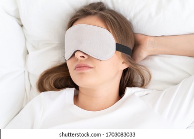 Headshot Of Young Woman Dreaming In Bed In Daytime, Wearing Gray Sleeping Mask Covering Eyes Fully, Relaxing After Night Shift Or Long Studies