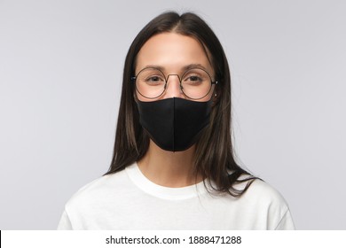 Headshot Of Young Woman Or Female Teacher In Round Glasses And Black Medical Mask, Looking At Camera With Smile, Isolated On Gray Background