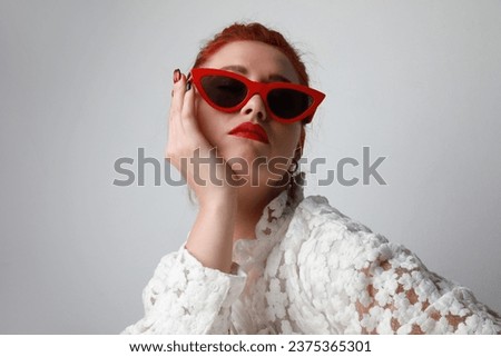 Headshot of young woman wearing cat-eye sunglasses posing on white background. 