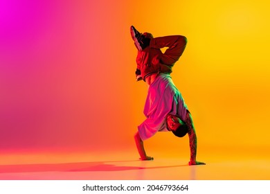 Headstand. Portrait of young stylish man, break dancing dancer training in casual clothes isolated over gradient pink yellow background. Youth culture, movement, street style and fashion, action. - Shutterstock ID 2046793664