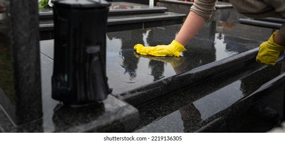Headstone cleaning on cemetery. Professional in yellow gloves cleans the marble grave, polishing marble tombstone with special liquid,  preparation for All Saints Day on November 1st - Shutterstock ID 2219136305