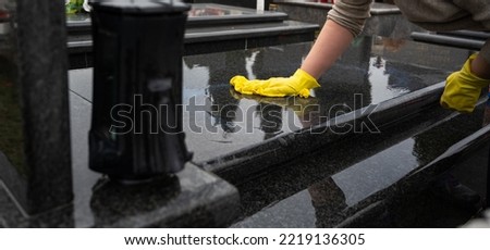 Headstone cleaning on cemetery. Professional in yellow gloves cleans the marble grave, polishing marble tombstone with special liquid,  preparation for All Saints Day on November 1st