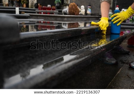 Headstone cleaning on cemetery. Professional in yellow gloves cleans the marble grave, polishing marble tombstone with special liquid,  preparation for All Saints Day on November 1st