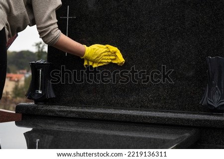 Headstone cleaning on cemetery. Professional in yellow gloves cleans the marble grave, polishing marble tombstone,   preparation for All Saints Day on November 1st