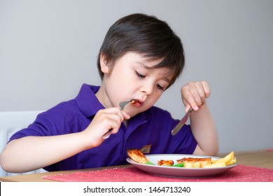 Healhty Kid Eating Homemade Salmon Steak And Chips For His Sunnday Dinner At Home, Portrait Of Child Boy Learning How To Use Knife And Fork By Him Self, Healthy Food For Children Concept