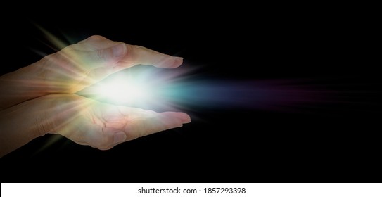 The Healing Hands Of A Lightworker - Female Parallel Hands Against Pitch Black Background With A Bright White Light Between Palms And Space For Message On Right Side
