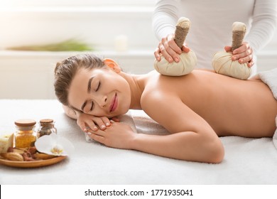 Healing herbal massage. Masseuse making relaxing body massage to young woman with herbal compress balls, spa interior