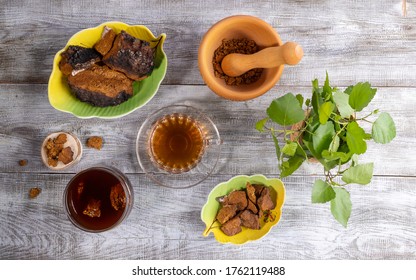Healing infusion from birch mushroom chaga, ingredients for its cooking and green birch twigs on wooden table. Chaga coffee or tea. Beverage improving immunity. Trendy superfood. Top view, flat lay.