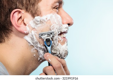 Health beauty and skin care concept. Closeup young bearded man with foam on face shaving with razor on blue background. - Powered by Shutterstock