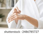 Health care, beauty asian young woman in bathrobe, towel after shower bath, spa relax at home, finger applying moisturizer on her back hand. Skin body cream moisturizing lotion, routine in morning.