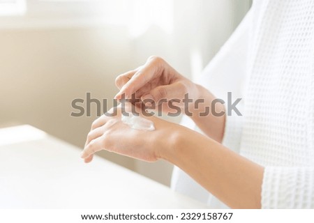 Health care, beauty asian young woman in bathrobe, towel after shower bath, spa relax at home, finger applying moisturizer on her back hand. Skin body cream moisturizing lotion, routine in morning.