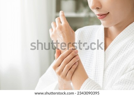 Health care, beauty smile pretty asian young woman in bathrobe, towel after shower bath at home, finger applying moisturizer on her back hand. Skin body cream moisturizing lotion, routine in morning.