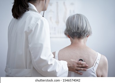 Health Care Concept: Female Doctor Auscultating The Lungs Of A Senior Long Covid Or Copd Patient With A Stethoscope.