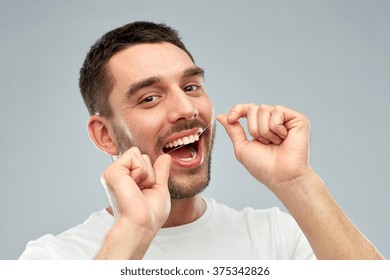 Health Care, Dental Hygiene, People And Beauty Concept - Smiling Young Man With Floss Cleaning Teeth Over Gray Background