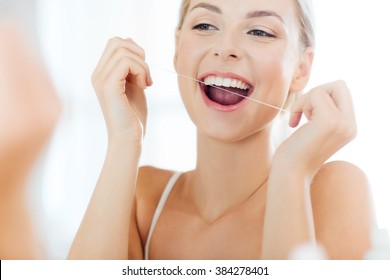 Health Care, Dental Hygiene, People And Beauty Concept - Smiling Young Woman With Floss Cleaning Teeth And Looking To Mirror At Home Bathroom