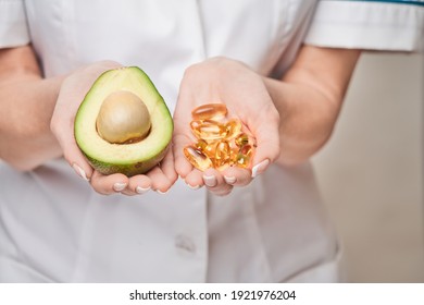 Health care and diet concept - doctor nutritionist or cardiologist holding fish oil in capsules for vitamin D and omega-3 fatty acids and avocado