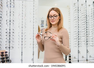 Health care, eyesight and vision concept - happy woman choosing glasses at optics store. Portrait of beautiful young woman trying new glasses in optician store - Powered by Shutterstock