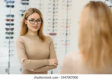 Health care, eyesight and vision concept - happy woman choosing glasses at optics store. Portrait of beautiful young woman trying new glasses in optician store - Powered by Shutterstock