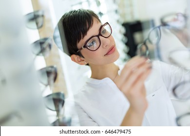 health care, eyesight and vision concept - happy woman choosing glasses at optics store - Powered by Shutterstock