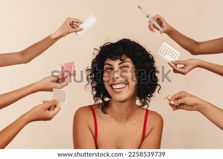 Health care and family planning options for women. Female smiling in studio with hands holding birth control. Woman making choices for her reproductive health, she is being offered different options.